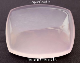 May include: A square, pale pink gemstone with gently curved edges. The polished surface reflects light, creating a soft glow. The gemstone is set against a dark background, with the text "JaipurGemUs" in white on the sides.