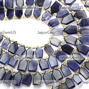 Op de afbeelding: Detailopname van een ketting of armband met donkerblauwe, geometrisch geslepen edelsteen kralen. De kralen worden gescheiden door kleine, goudkleurige afstandhouders. De edelstenen zijn gefacetteerd.