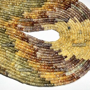 May include: Strands of gemstone beads in shades of yellow, brown, and green. The beads are small and round, with a slightly faceted appearance. The beads are strung together, forming a circular shape. The image has the text "JaipurGemUS" in multiple places.