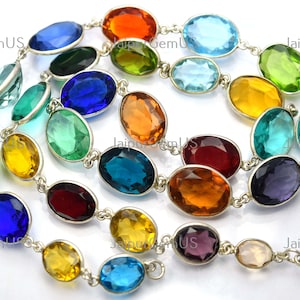 May include: A colorful necklace featuring oval-shaped gemstones in various colors, including blue, green, yellow, and orange. The gemstones are linked together with a silver chain, creating a vibrant and eye-catching accessory.