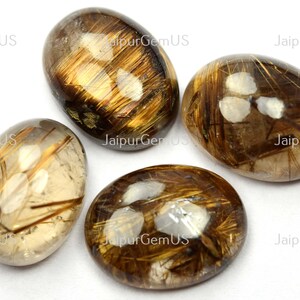 May include: Four oval-shaped gemstones with a translucent, golden-brown hue. The stones feature internal inclusions of golden, hair-like structures. The gemstones are polished and smooth, with a reflective surface. The overall aesthetic is natural and earthy.