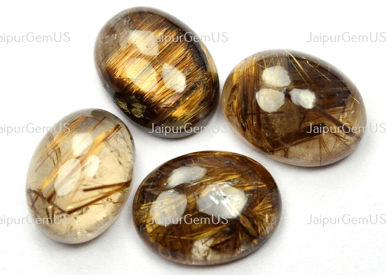 May include: Four oval-shaped gemstones with a translucent, golden-brown hue. The stones feature internal inclusions of golden, hair-like structures. The gemstones are polished and smooth, with a reflective surface. The overall aesthetic is natural and earthy.