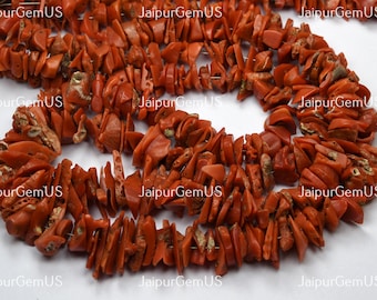 May include: Strands of natural, reddish-orange coral chips. The coral pieces are irregular in shape and size, strung together to form a necklace or bracelet. The image is well-lit, showing the texture and color variations of the coral. The text "JaipurGemUS" is visible.