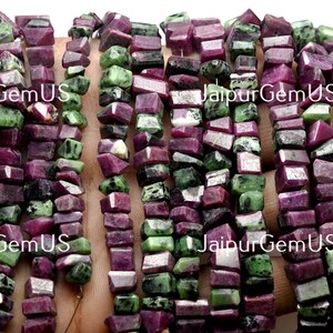 Puede incluir: Hebras de cuentas de piedras preciosas de rub&iacute; y zoisita en bruto. Las cuentas son una mezcla de colores rojo intenso y verde, con un corte rugoso e irregular. Las cuentas est&aacute;n ensartadas, listas para la fabricaci&oacute;n de joyas. El texto "JaipurGemUS" es visible.