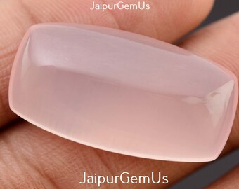 May include: A polished, rectangular gemstone with rounded corners, showing a soft, translucent pink hue. The gemstone is held in a hand, showcasing its smooth, reflective surface. The overall shape is a rectangle with slightly curved sides.
