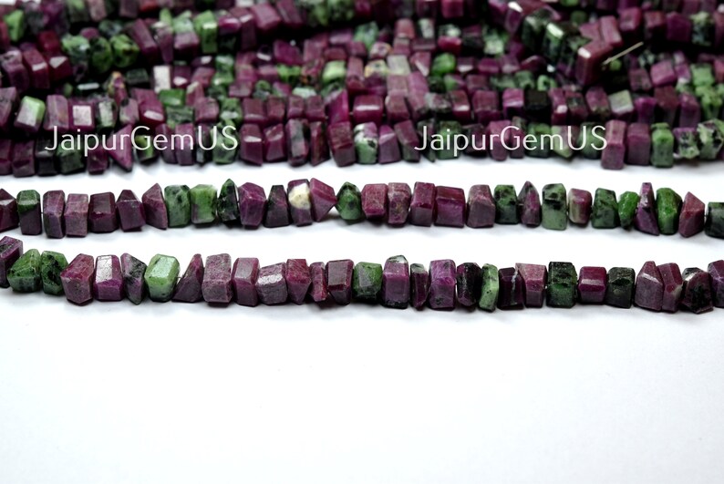 Puede incluir: Hebras de cuentas de piedras preciosas de rub&iacute; y zoisita en bruto. Las cuentas son una mezcla de colores rojo intenso y verde, cortadas en formas rectangulares irregulares. El texto "JaipurGemUS" es visible en la imagen.