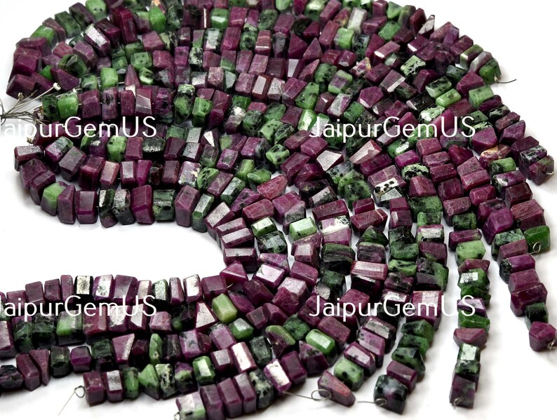 Puede incluir: Hebras de cuentas de piedras preciosas en tonos rojo oscuro y verde. Las cuentas son de forma aproximadamente rectangular y parecen estar cortadas de piedra natural. El texto "JaipurGemUS" es visible. Estas cuentas probablemente se utilizan para la fabricaci&oacute;n de joyas.