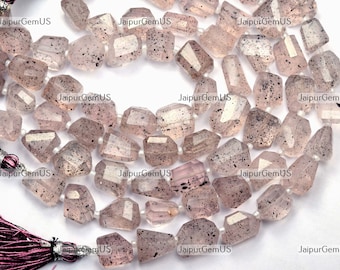 May include: Strand of faceted, light pink gemstone beads with dark speckles. The beads are strung together, and a tassel is visible on the left side. The beads are approximately 1 cm in size.