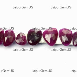 Peut inclure: Collection de sept pierres précieuses rubis rouge foncé, facettées. Chaque pierre a une forme unique, comme des poires, des ovales et des formes irrégulières. Les pierres sont présentées sur une surface blanche, avec le texte "JaipurGemUS" en arrière-plan.