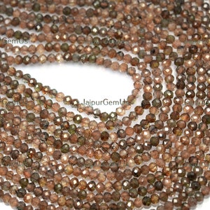 May include: Strands of faceted, round beads in shades of brown and olive green. The beads are small and appear to be strung together, creating a textured surface. The beads are likely used for jewelry making or crafting.
