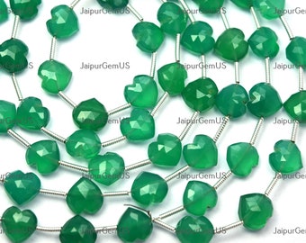 Puede incluir: Primer plano de hileras de piedras preciosas verdes facetadas en forma de corazón ensartadas en alambre de plata. Las piedras tienen una superficie pulida. La imagen está bien iluminada, mostrando el color vibrante y los cortes intrincados. El texto "JaipurGemUS" es visible.