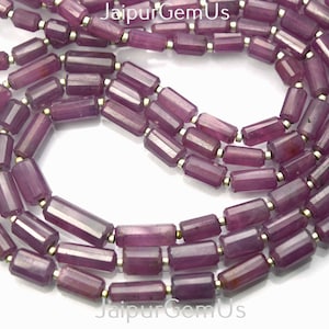 Könnte beinhalten: Stränge aus facettierten, zylindrischen Rubinperlen mit goldfarbenen Abstandshaltern. Die Perlen haben eine tiefe, purpurrote Farbe und sind zu einer Halskette oder einem Armband aufgereiht.