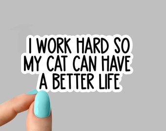 May include: White sticker with black text that reads "I work hard so my cat can have a better life". The sticker is being held by a hand with light blue nail polish.