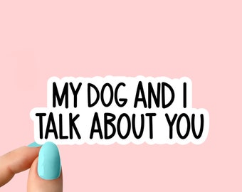 Op de afbeelding: Witte sticker met zwarte tekst die "Mijn hond en ik praten over jou" zegt. Een hand houdt de sticker vast.