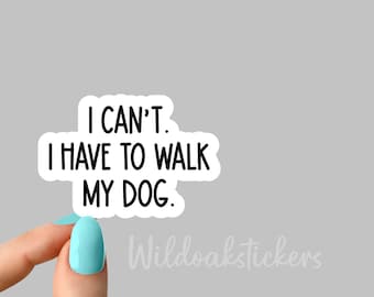 Op de afbeelding: Een witte sticker met zwarte tekst die "Ik kan niet. Ik moet mijn hond uitlaten." luidt. De sticker wordt vastgehouden door een vinger met lichtblauwe nagellak.
