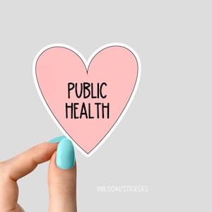 May include: A pink heart-shaped sticker with the text "PUBLIC HEALTH" in black lettering. The sticker is being held by a hand with light blue nail polish.