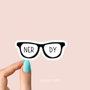 May include: A black and white sticker of a pair of glasses with the words "NERDY" written on the lenses. The sticker is being held by a hand with light blue nail polish.