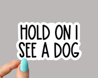 Op de afbeelding: Witte sticker met zwarte tekst die "Hold on I see a dog" zegt.