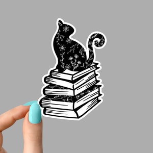 May include: Black silhouette of a cat with white floral details sitting on top of a stack of five books. The cat's tail curls around the books.
