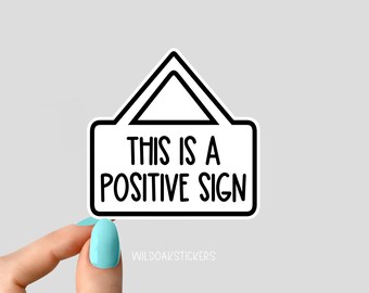 May include: White sticker with black outline in the shape of a triangle with rounded corners. The sticker says "This is a Positive Sign".