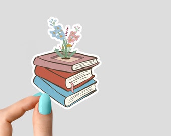 May include: A stack of three books with a small flower arrangement growing out of the top book. The books are pink, red, and blue.