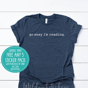 May include: A navy blue t-shirt with the text "go away i'm reading." printed in white. A teal circle sticker with white text says "Limited Time! Free Any 5 Sticker Pack with purchase of shirt. Use code FREESTICKERS."