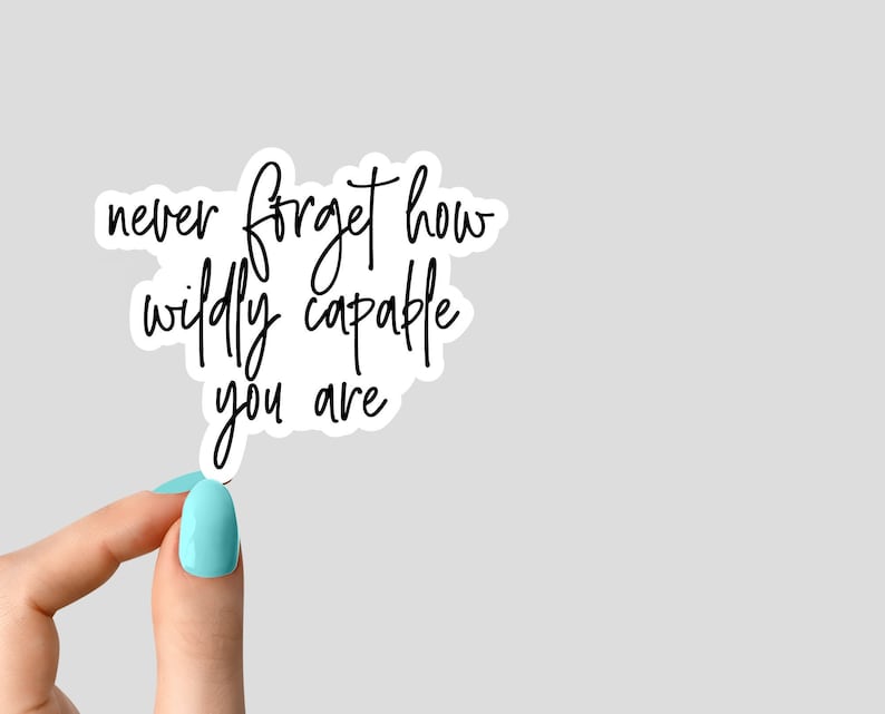 May include: A white sticker with black lettering that reads "never forget how wildly capable you are". A hand is holding the sticker.
