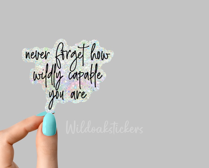 May include: A holographic sticker with the text "never forget how wildly capable you are". The sticker is being held by a hand with light blue nail polish.