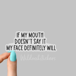 May include: White sticker with black text that reads "If my mouth doesn't say it my face definitely will." The sticker is being held by a hand with light blue nail polish. The text "Wildoakstickers" is visible in the bottom right corner.