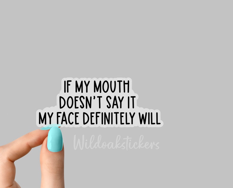 May include: White sticker with black text that reads "If my mouth doesn't say it my face definitely will." The sticker is being held by a hand with light blue nail polish. The text "Wildoakstickers" is visible in the bottom right corner.