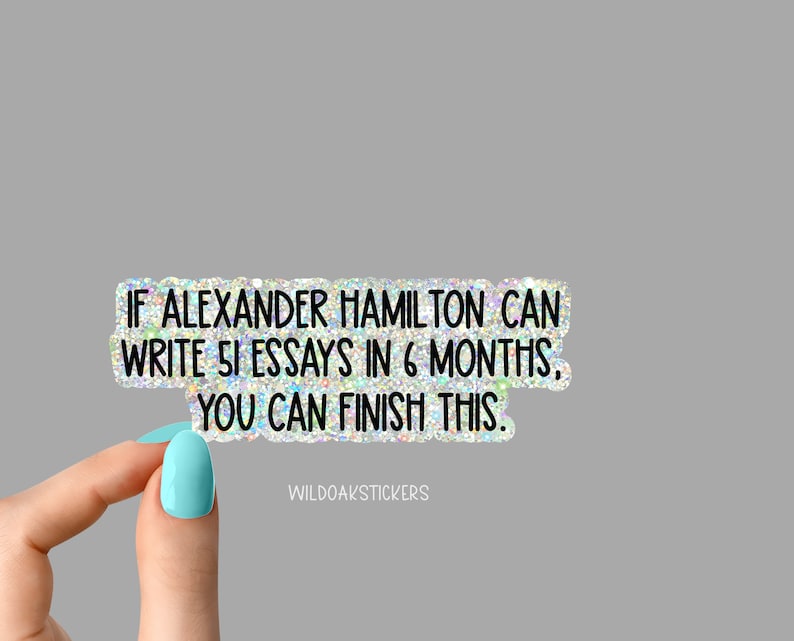 K&ouml;nnte beinhalten: Ein Aufkleber mit glitzerndem, schimmerndem Hintergrund und schwarzem Text, der "IF ALEXANDER HAMILTON CAN WRITE 51 ESSAYS IN 6 MONTHS, YOU CAN FINISH THIS." lautet. Der Aufkleber wird von einer Hand mit hellblauem Nagellack gehalten.
