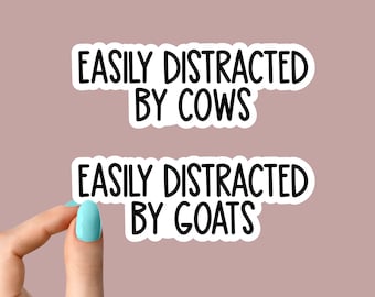 May include: Two white stickers with black text. The top sticker says "Easily Distracted By Cows". The bottom sticker says "Easily Distracted By Goats".
