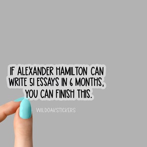 K&ouml;nnte beinhalten: Ein wei&szlig;er Aufkleber mit schwarzem Text, der lautet: "Wenn Alexander Hamilton 51 Essays in 6 Monaten schreiben kann, kannst du das auch schaffen." Der Aufkleber wird von einer Hand mit hellblauem Nagellack gehalten. Der Text "WILDOAKSTICKERS" befindet sich am unteren Rand des Aufklebers.