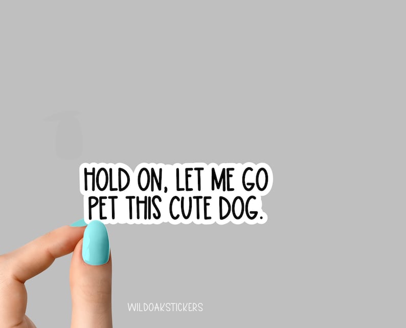 May include: White sticker with black text that reads "Hold on, let me go pet this cute dog." The sticker is being held by a hand with light blue nail polish.
