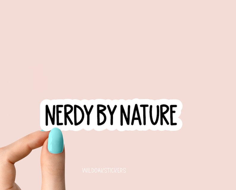 以下が含まれることがあります： 「Nerdy by Nature」という黒い文字が書かれた白いステッカー。手がステッカーを持っています。
