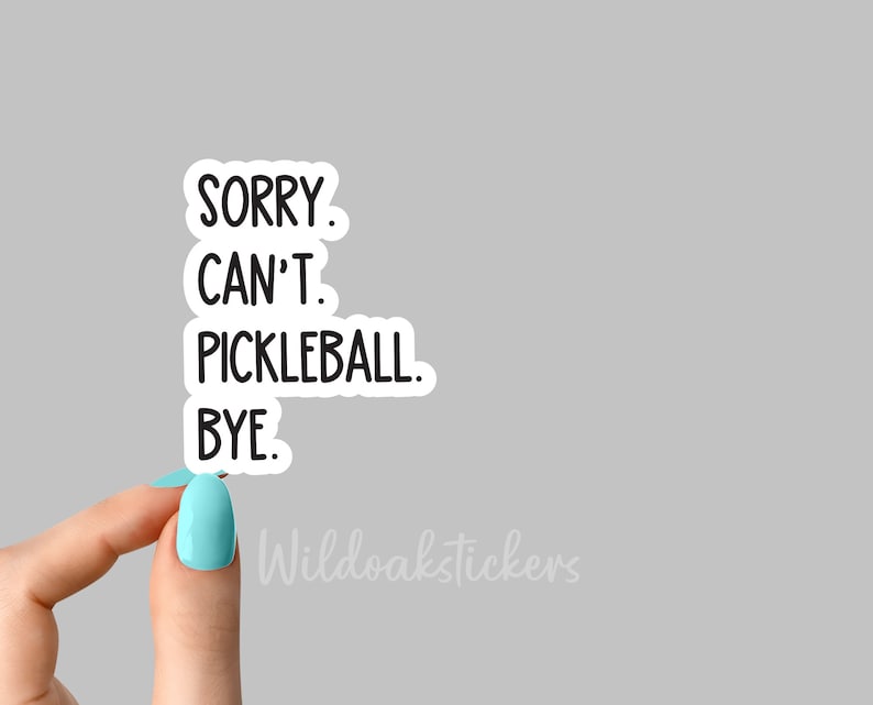 May include: A white sticker with black text that reads "SORRY. CAN'T. PICKLEBALL. BYE." The sticker is being held by a hand with light blue nail polish.