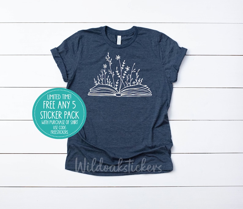 May include: A navy blue t-shirt with a white outline of an open book with flowers growing from the pages. The text "LIMITED TIME! FREE ANY 5 STICKER PACK WITH PURCHASE OF SHIRT USE CODE FREESTICKERS" is on a teal circle sticker.