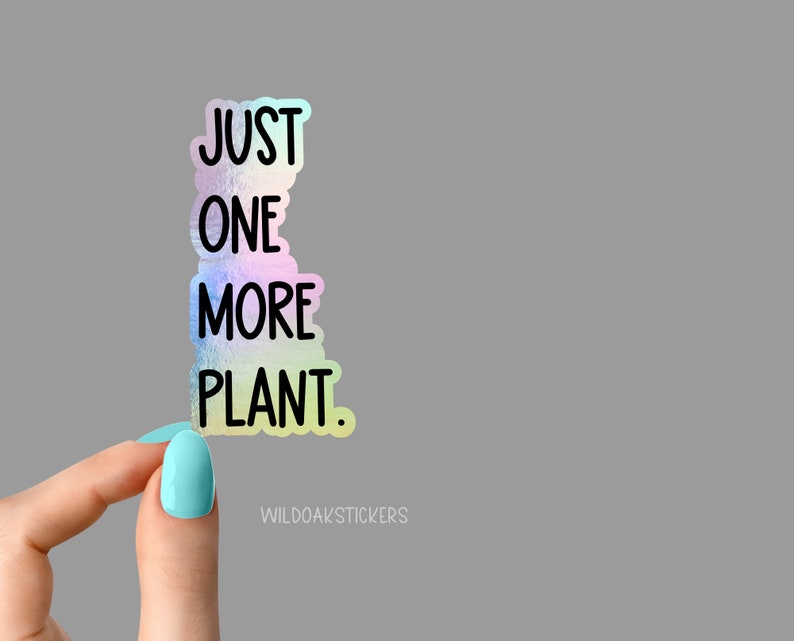 May include: A holographic sticker with the text "JUST ONE MORE PLANT." The sticker is being held by a hand with light blue nail polish.