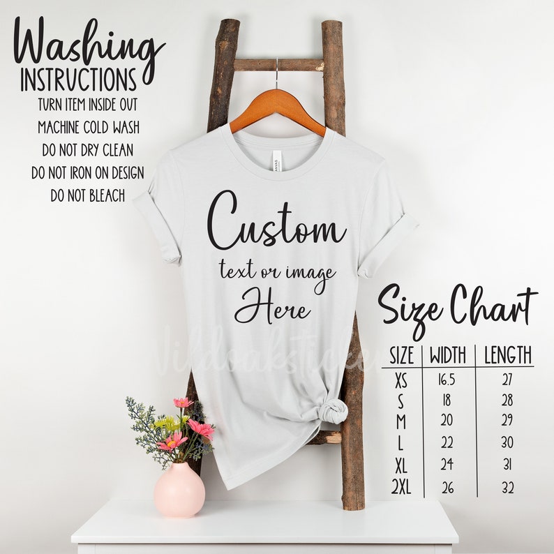 May include: A light gray t-shirt with the text "Custom text or image Here" printed on the front. A size chart is shown with measurements in inches. The shirt is hanging on a wooden ladder.