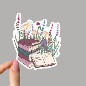 May include: A stack of books with a single book open on top. The books are surrounded by a variety of colorful flowers, including purple, pink, and yellow.