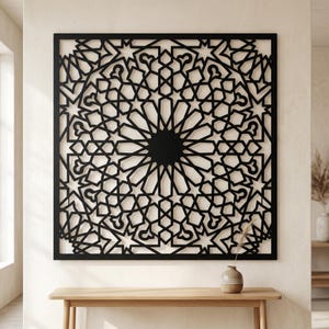 Peut inclure: Une décoration murale carrée noire présentant un motif géométrique complexe avec des formes d'étoiles et de polygones répétées. Le design est enfermé dans un cadre noir solide, créant une structure en treillis ajourée et symétrique.