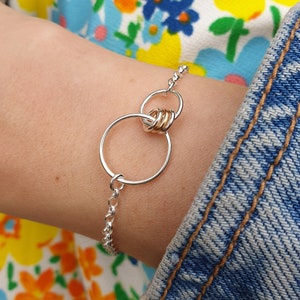 May include: A silver chain bracelet with a gold and silver circle design. The circles are interlocked and the gold circle is made of multiple smaller circles.