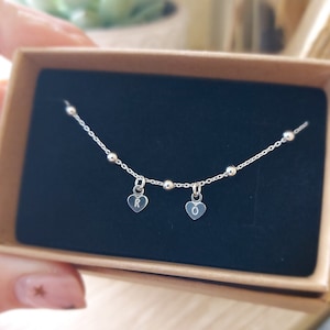 May include: A silver chain necklace with small silver beads and two heart-shaped charms. The charms are engraved with the letters "R" and "O".