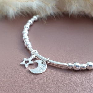 May include: A silver beaded bracelet with a moon and star charm. The moon charm can be personalised on the reverse.