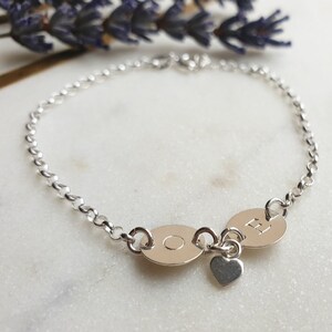 May include: A silver chain bracelet with two round charms, one with the letter "O" and the other with the letter "E", and a small heart charm.