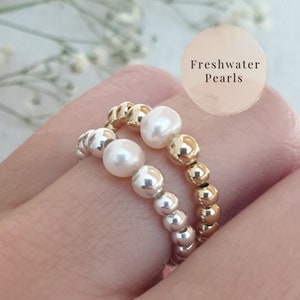 May include: Two rings with freshwater pearls and gold and silver beads. The rings are stacked on top of each other.
