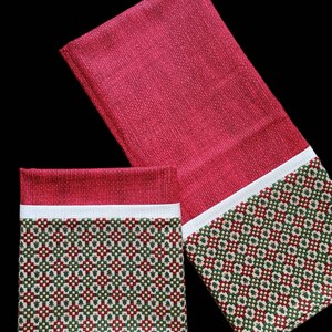 May include: Two red and white Christmas-themed tea towels with a green and red pattern of small Christmas trees. The towels have a white border.