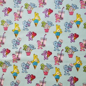 May include: A light blue fabric with a repeating pattern of cartoon bears holding ice cream cones, cupcakes, and bubble tea. The bears are in various colors, including yellow, blue, purple, and green.