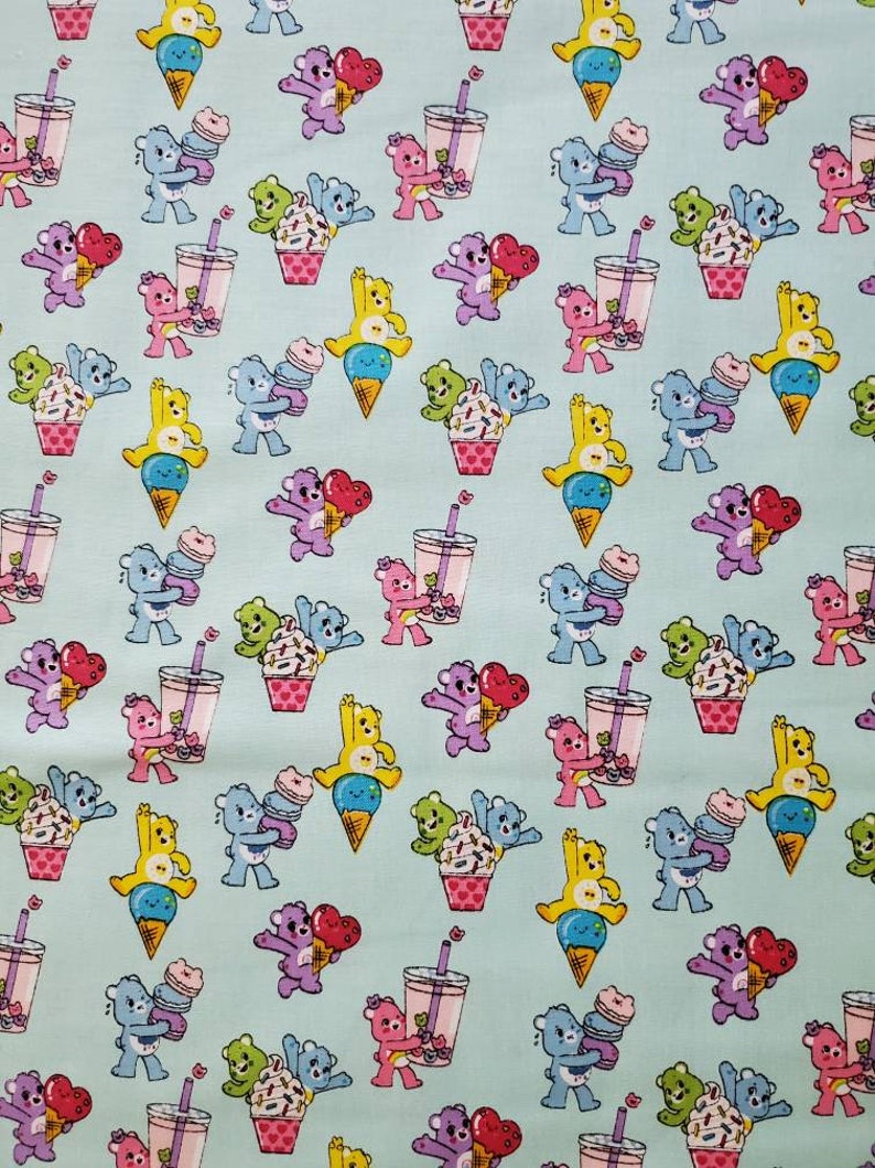 May include: A light blue fabric with a repeating pattern of cartoon bears holding ice cream cones, cupcakes, and bubble tea. The bears are in various colors, including yellow, blue, purple, and green.