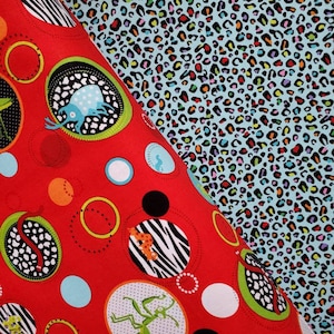 May include: Red fabric with a repeating pattern of circles containing various animal illustrations, including a praying mantis, a snake, a beetle, and a zebra. The background is a light blue fabric with a leopard print.